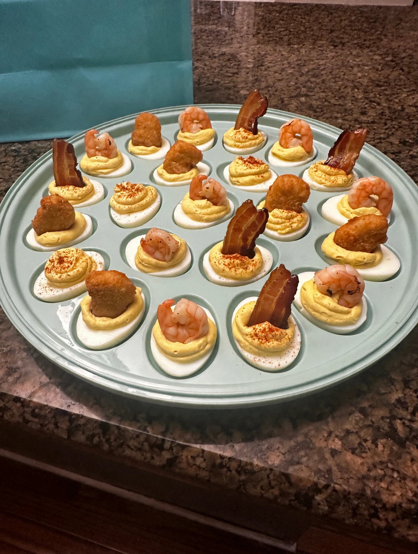 Deviled eggs with paprika, shrimp, fried chicken and candied bacon toppings on a Tiffany blue platter